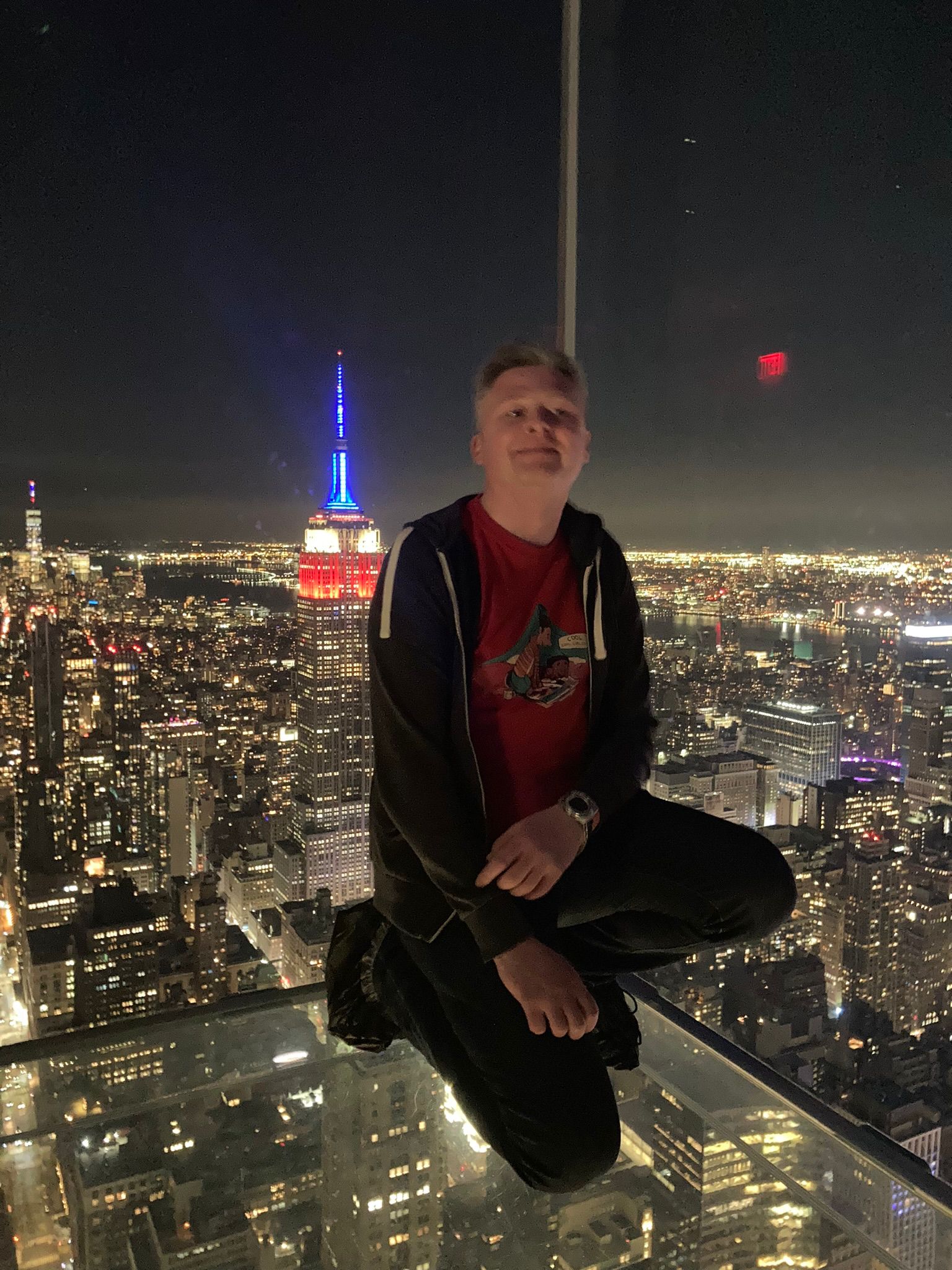 A man in a red tshirt and dark jeans poses at Summit at One Vanderbilt