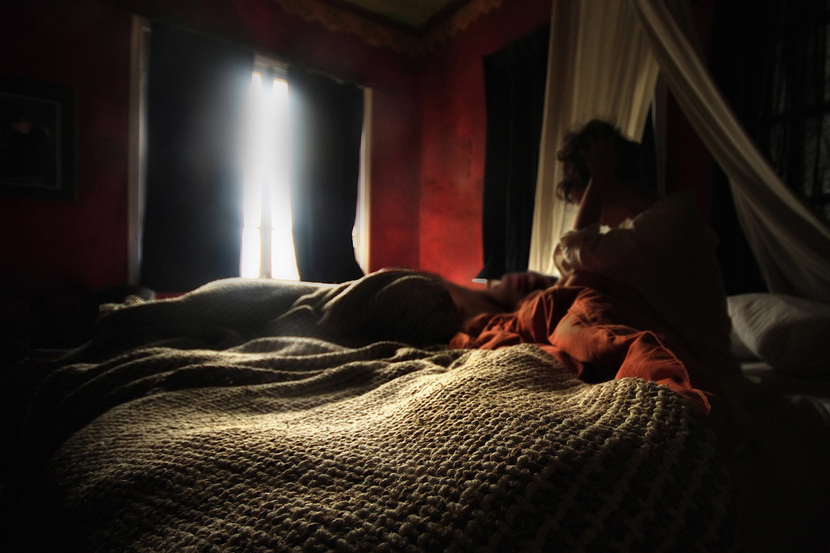 Light pours through a gap in the window as a woman watches their partner sleeping