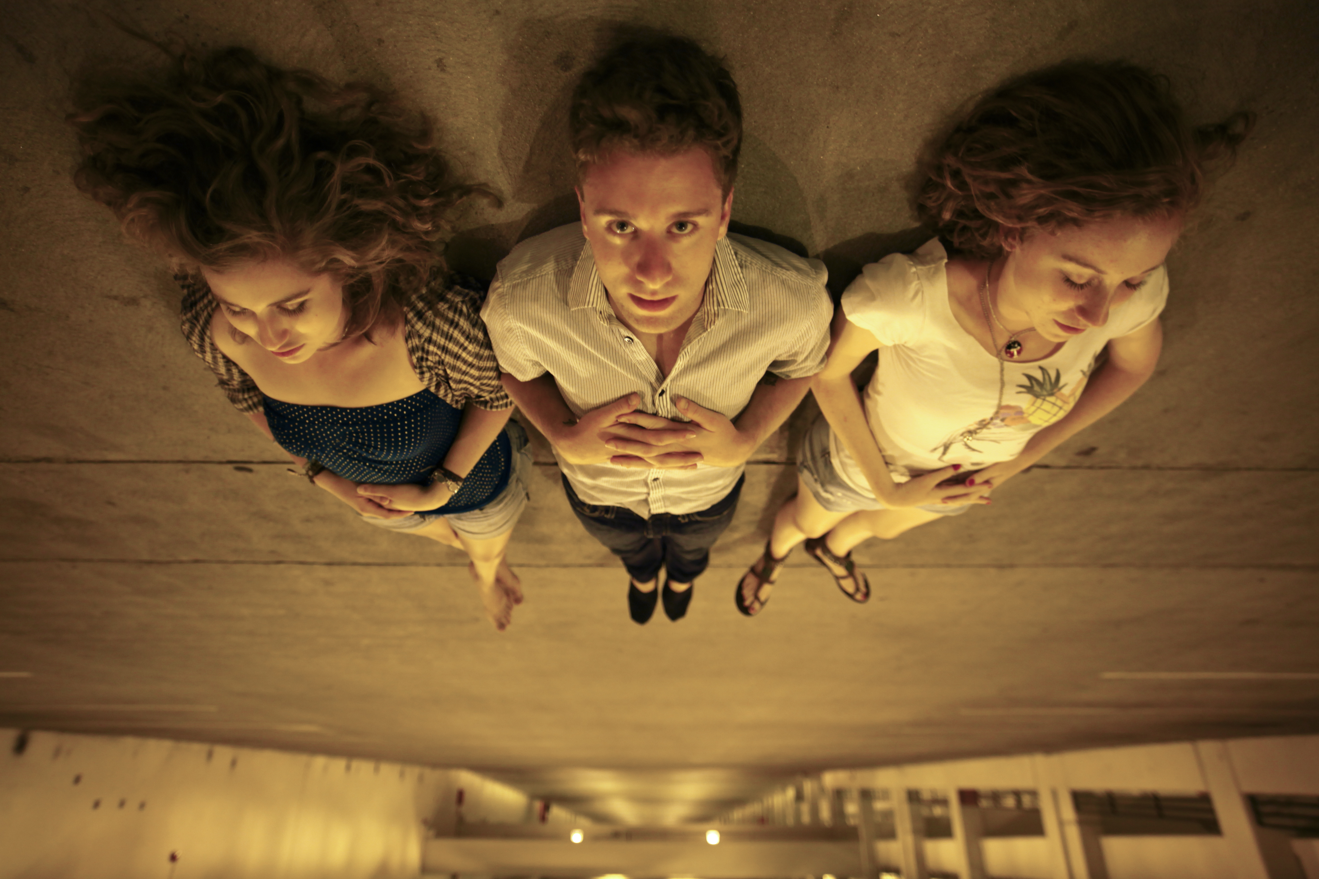 Two women and a man are sleeping on what seems to be the roof of a car park - well, the women are but the man is looking directly at the camera