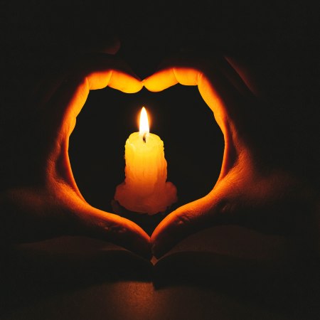 Heart-shaped hands and flame candle in darkness