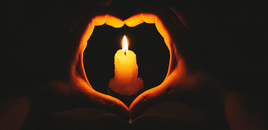 Heart-shaped hands and flame candle in darkness