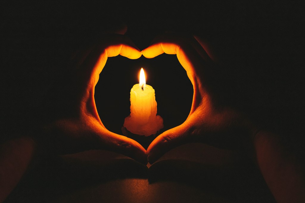Heart-shaped hands and flame candle in darkness