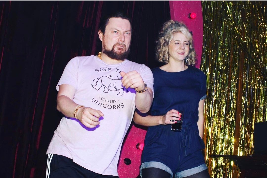 A man in a Save the Chubby Unicorn t-shirt dances with a woman in a dark blue dress