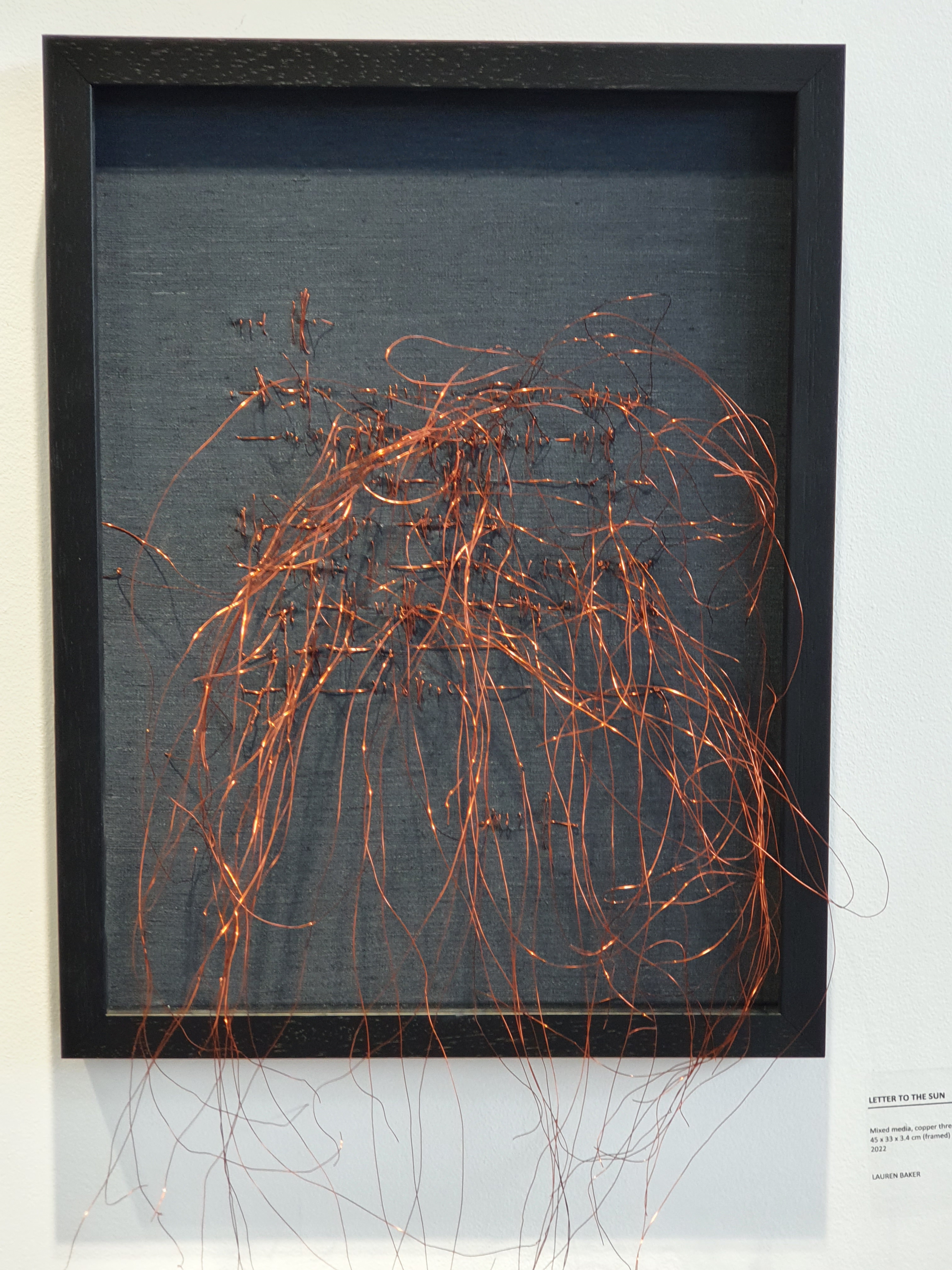 Glistening copper thread bursts out of the speckled grey canvas like sunbeams