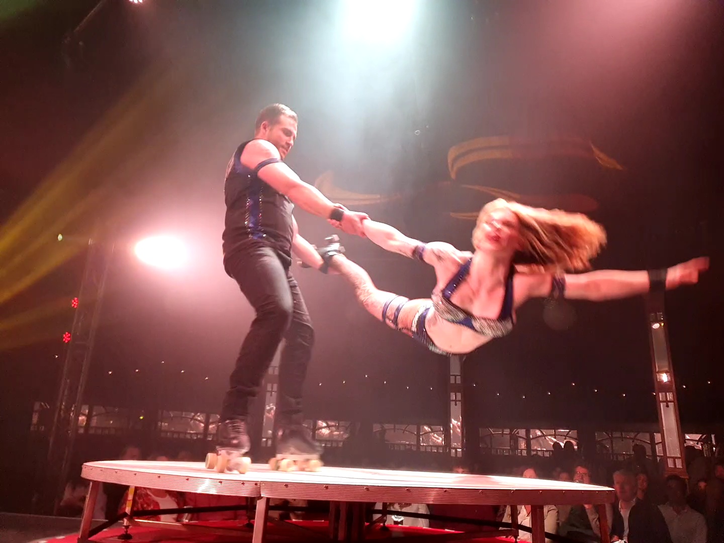The woman from The Skating Willers is being held by a leg and an arm as the man skates on the platform