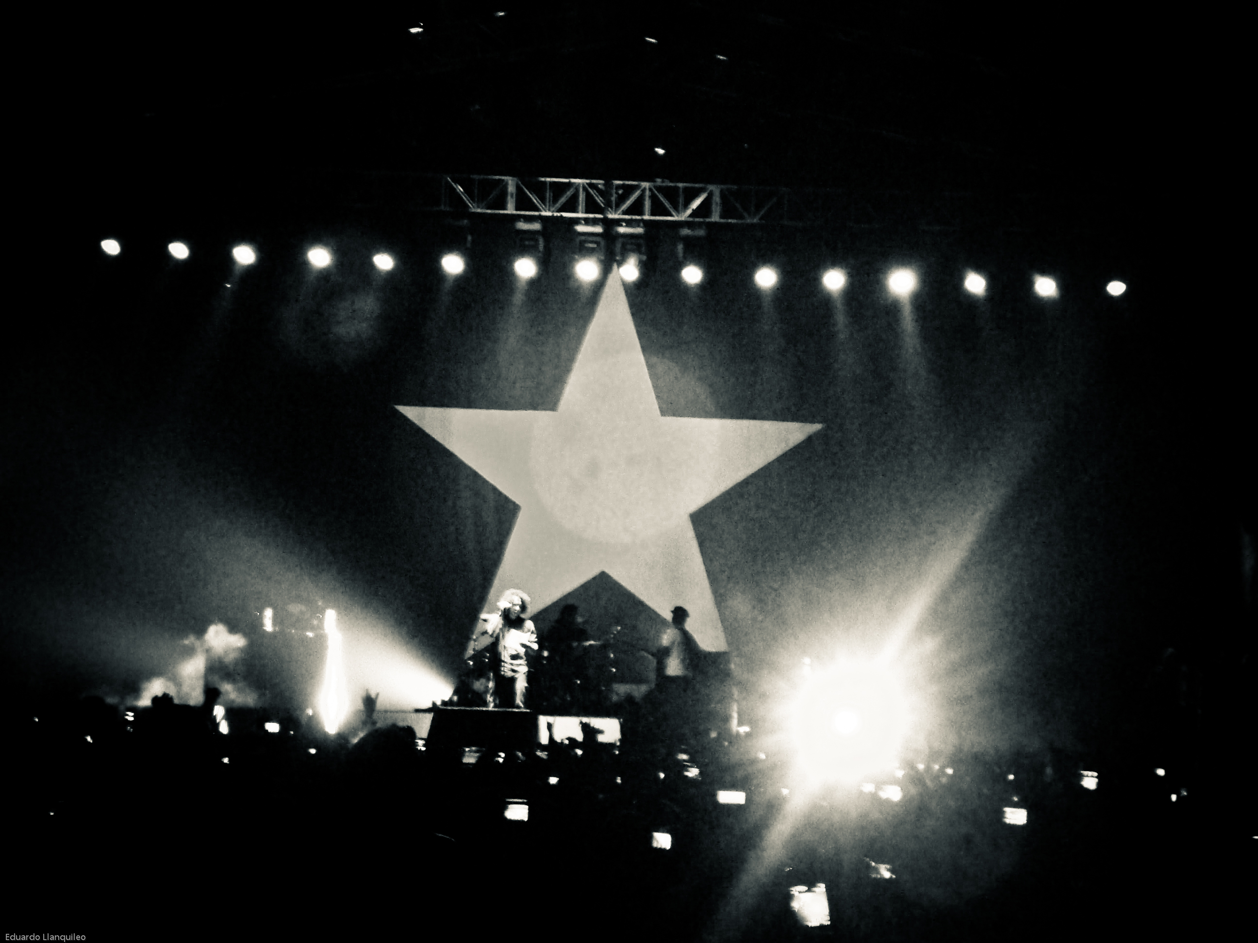 Rage Against the Machine are on stage in a black and white photo with a big star as the backdrop