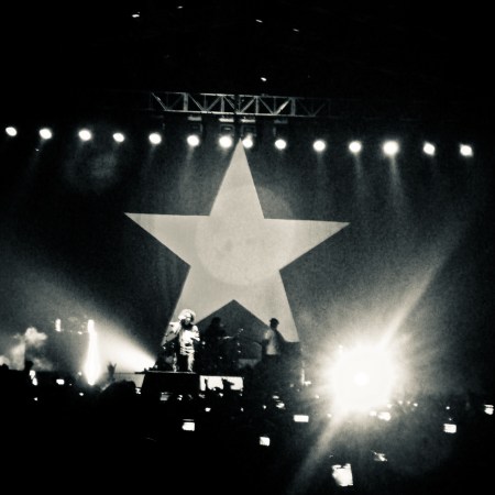 Rage Against the Machine are on stage in a black and white photo with a big star as the backdrop