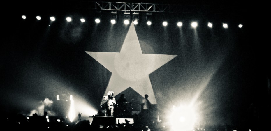 Rage Against the Machine are on stage in a black and white photo with a big star as the backdrop