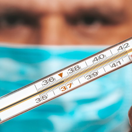 A man in a blue mask holds a thermometer