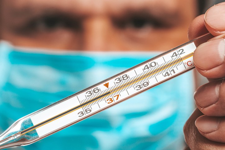 A man in a blue mask holds a thermometer